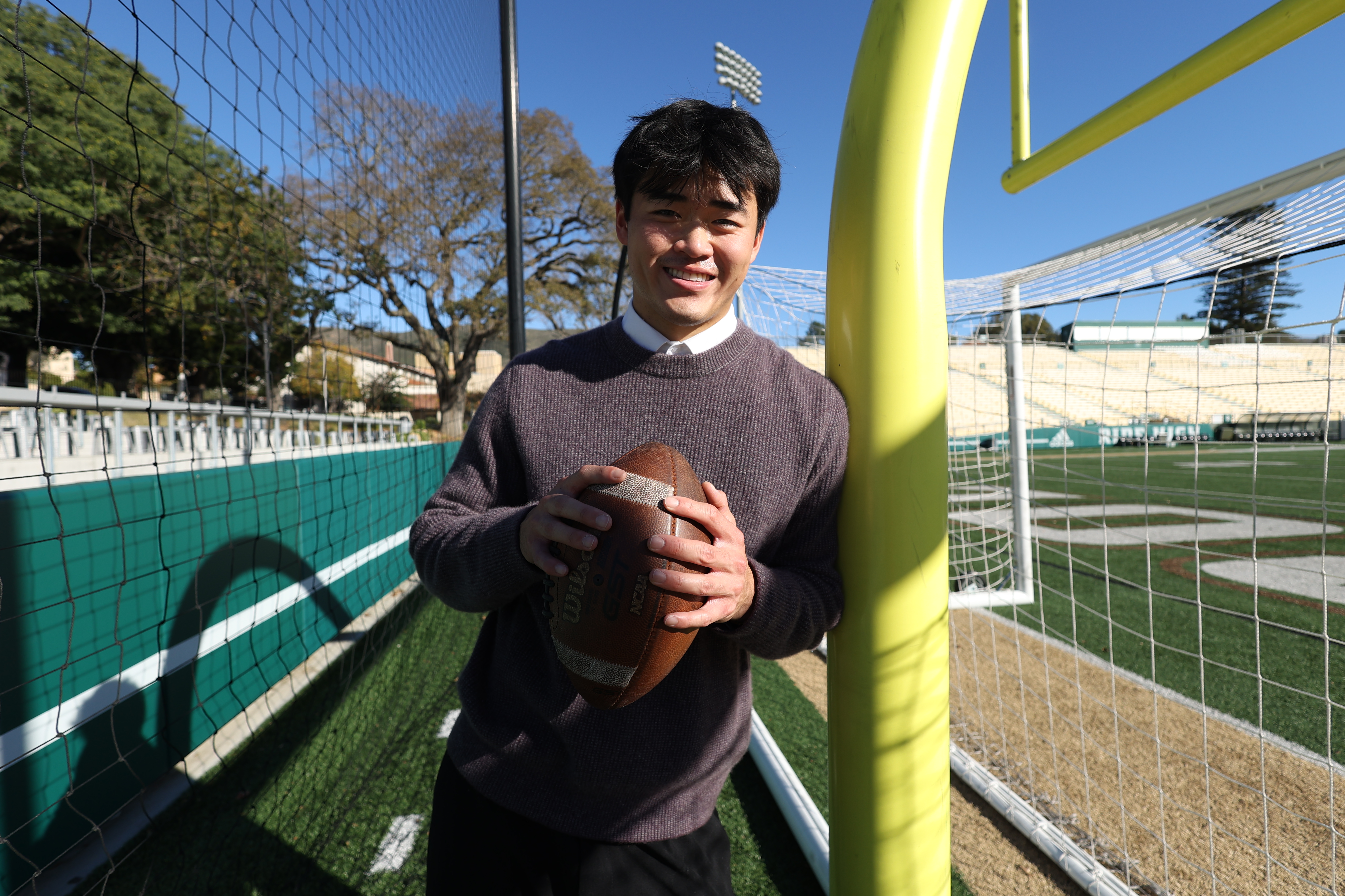 Spencer Zhang holds a football on the Cal Poly football field for a portrait