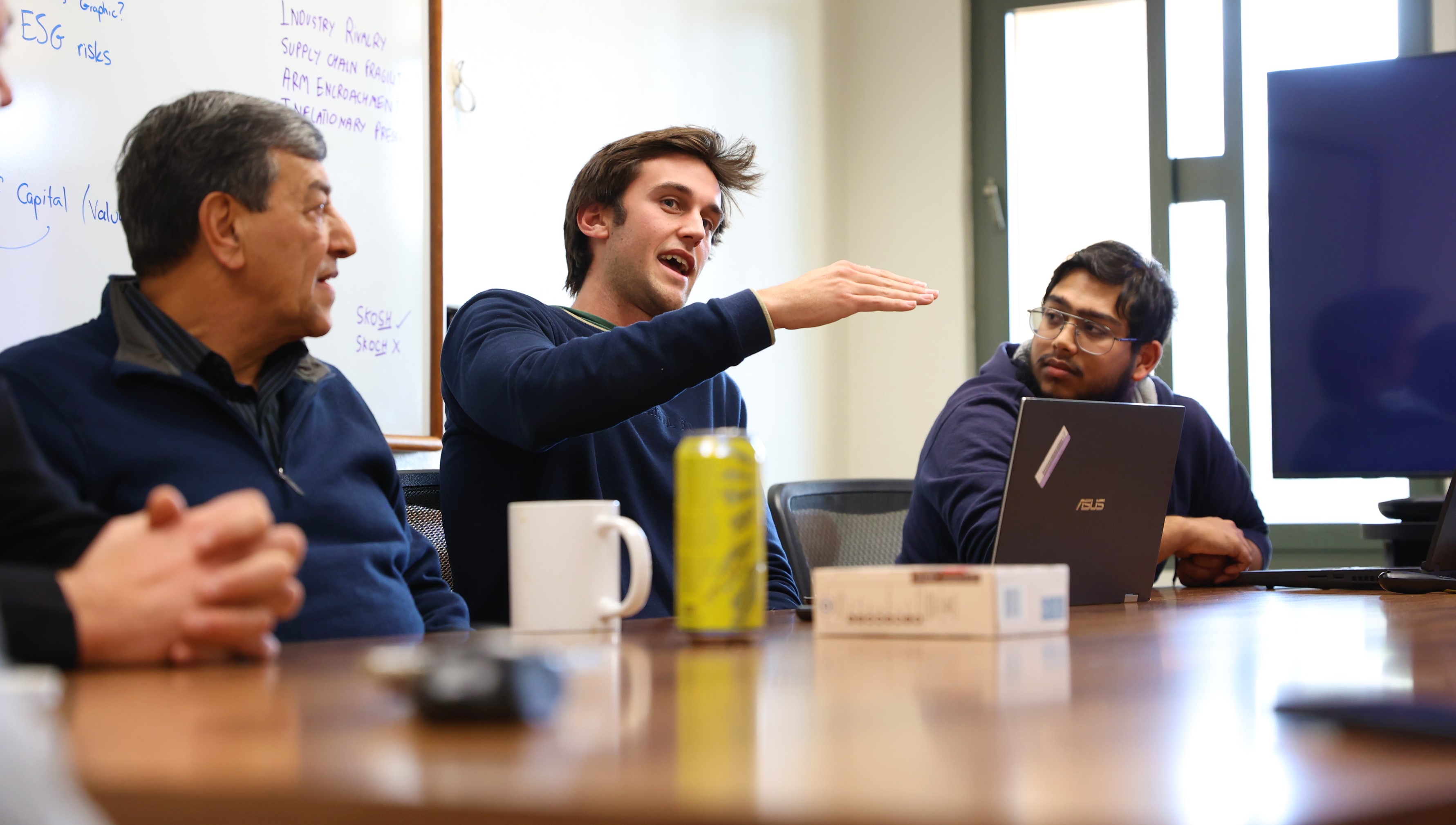 Finance students discuss a competition with a professor in a conference room