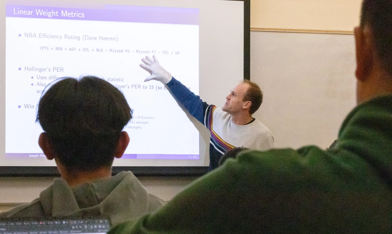 A professor points to a screen projecting a powerpoint in class