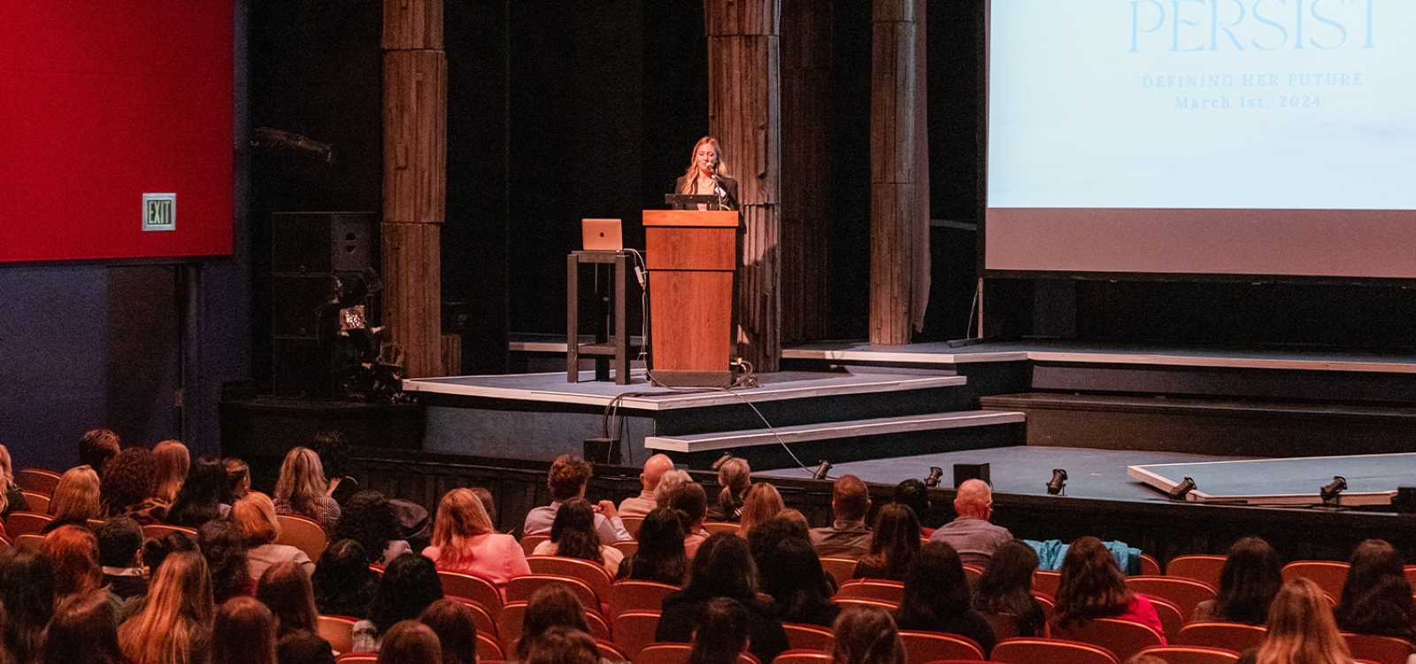 Speaker on a stage addressing the audience at the Defining Her Future conference