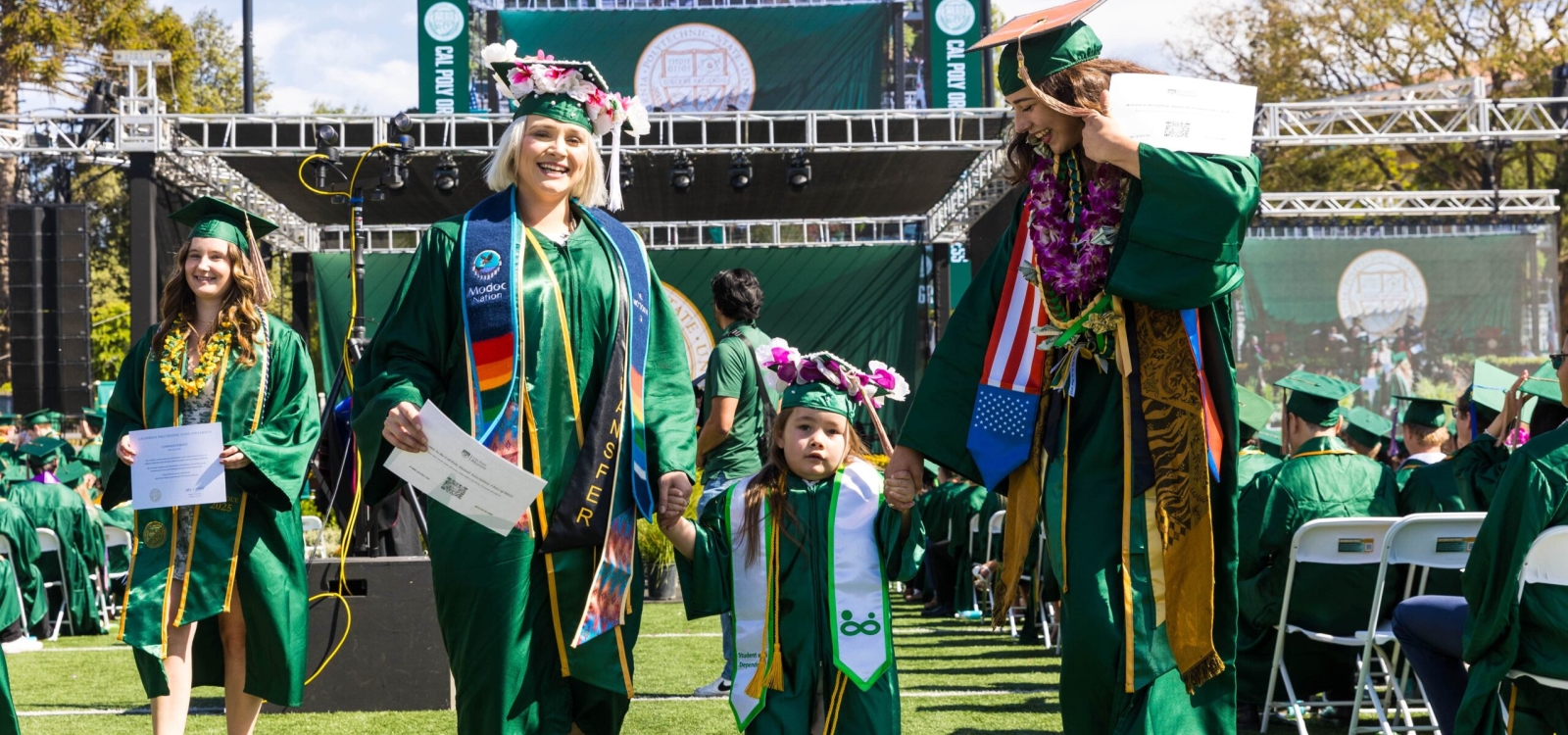 Two graduates holding the hands of a young girl walking between them