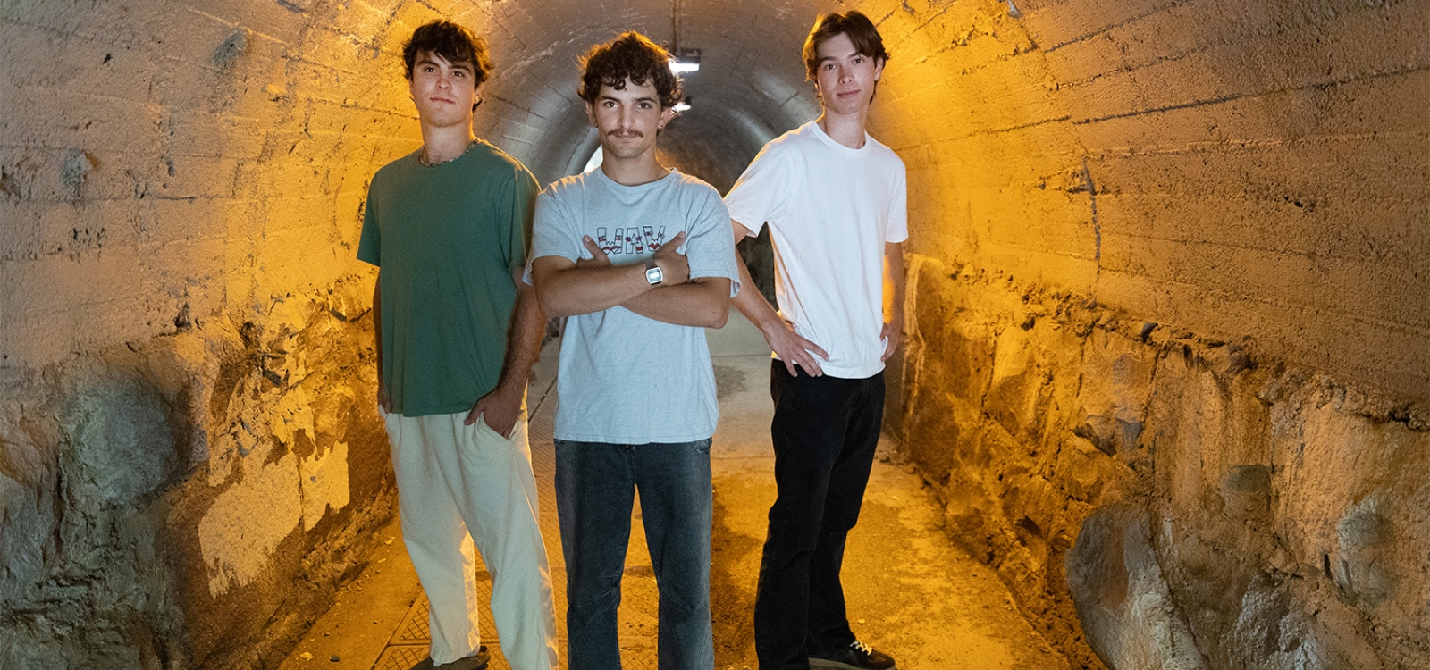 Three students pose for a portrait in a tunnel