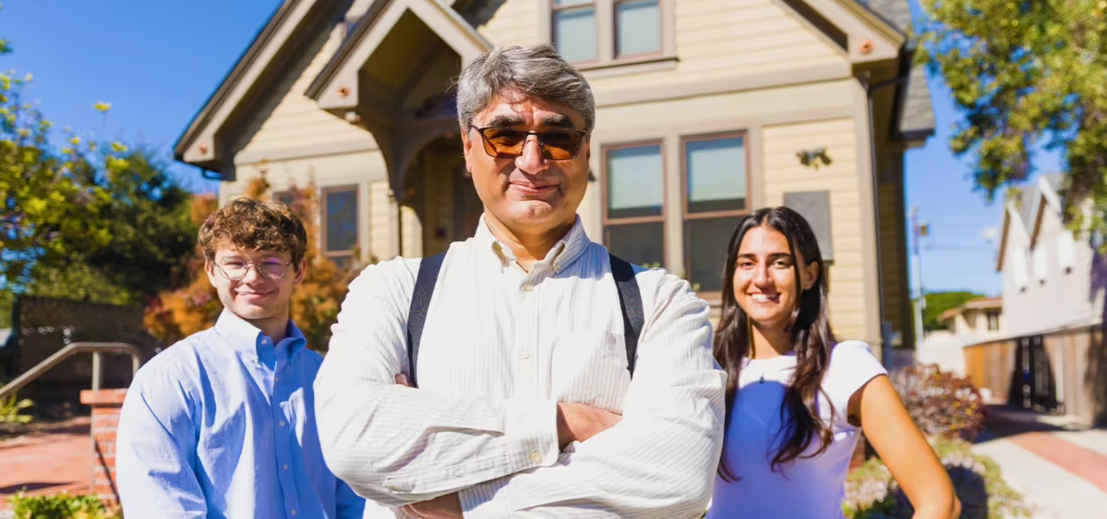 A professor and two students pose for a portrait outside a home