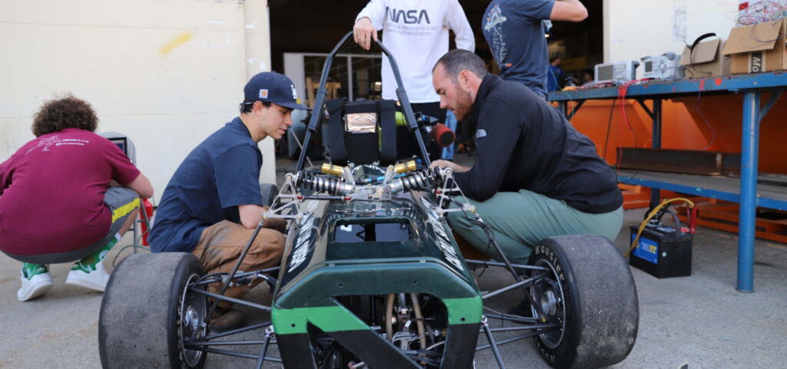Finance student Chase Gioffredi (center, with NASA shirt) inspects a Formula race car with mechanical engineering student Joe Watanabe (left side of car) and aerospace engineering major Alex Simonic.