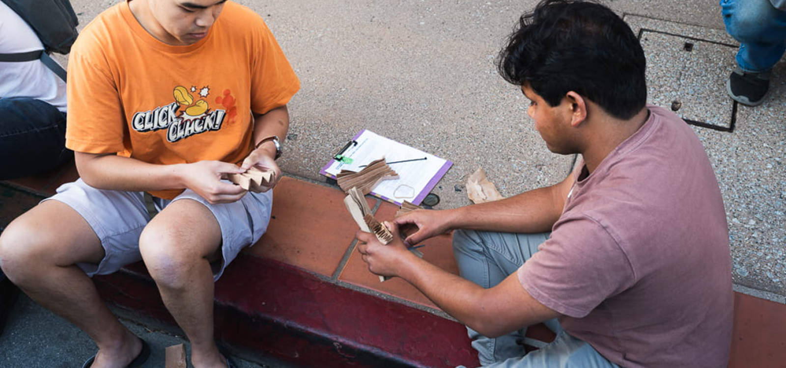 Two students prepare an egg package while sitting on a curb