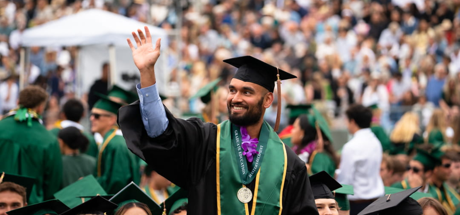 A graduating masters student waves toward the crowd at commencement
