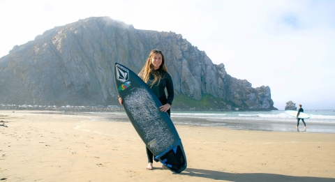 Maya Karl standing on the beach with her surfboard
