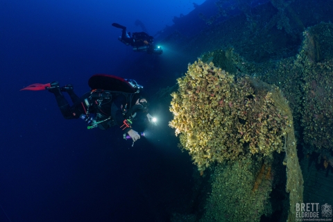 Divers explore a shipwreck's propeller