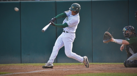Taison Corio hits a pitch during a game, with the catcher and umpire behind home plate.