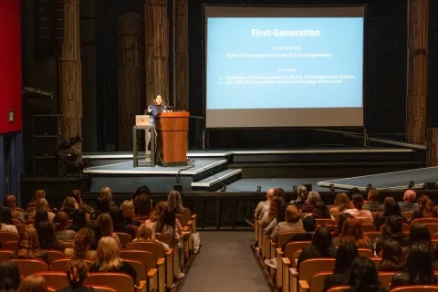 A crowd sits and listens to a speaker on a stage behind a podium