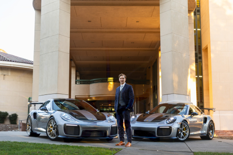 Elijah Shanks poses with two Porsches in front of the Cal Poly business building