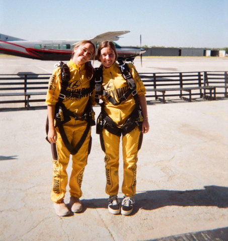 Two students at an airport, suited up for skydiving in Europe