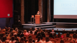 Speaker on a stage addressing the audience at the Defining Her Future conference