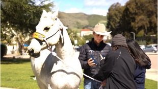 A rodeo athlete talks with students as he stands next to his horse