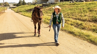 A rodeo member walks her horse down a trail