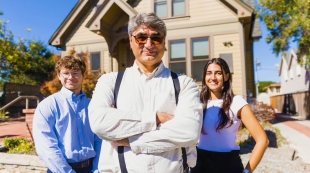 A professor and two students pose for a portrait outside a home