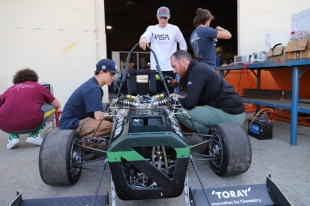 Finance student Chase Gioffredi (center, with NASA shirt) inspects a Formula race car with mechanical engineering student Joe Watanabe (left side of car) and aerospace engineering major Alex Simonic.