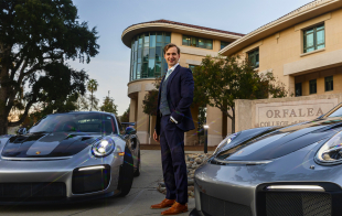 Alumni poses with two Porsches outside business building