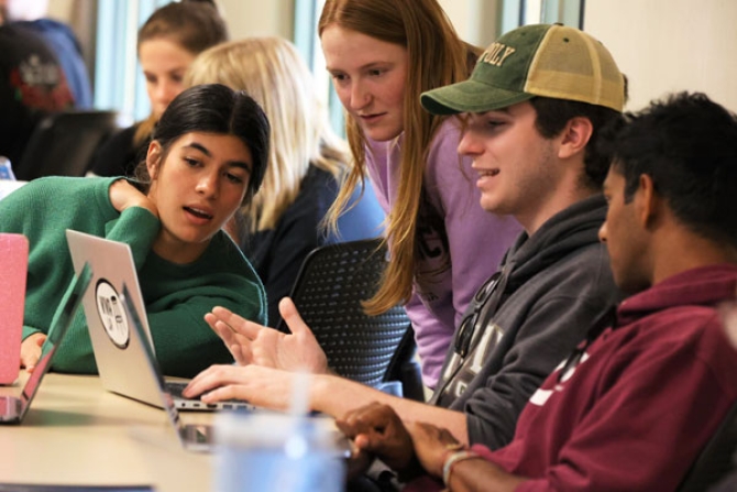 Students huddling around and viewing content on a laptop