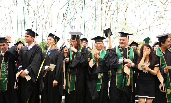 Graduates at commencement celebrating, streamers on the air above them