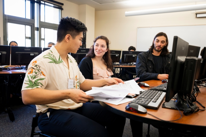 two male and one female students at desk reviewing documents