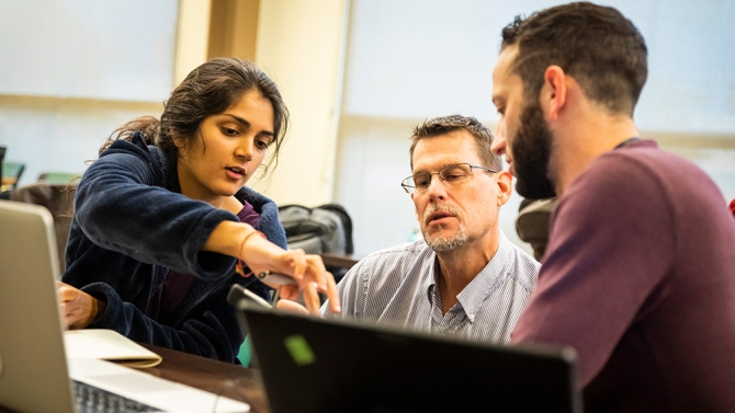 Students talking to teacher in front of laptop 