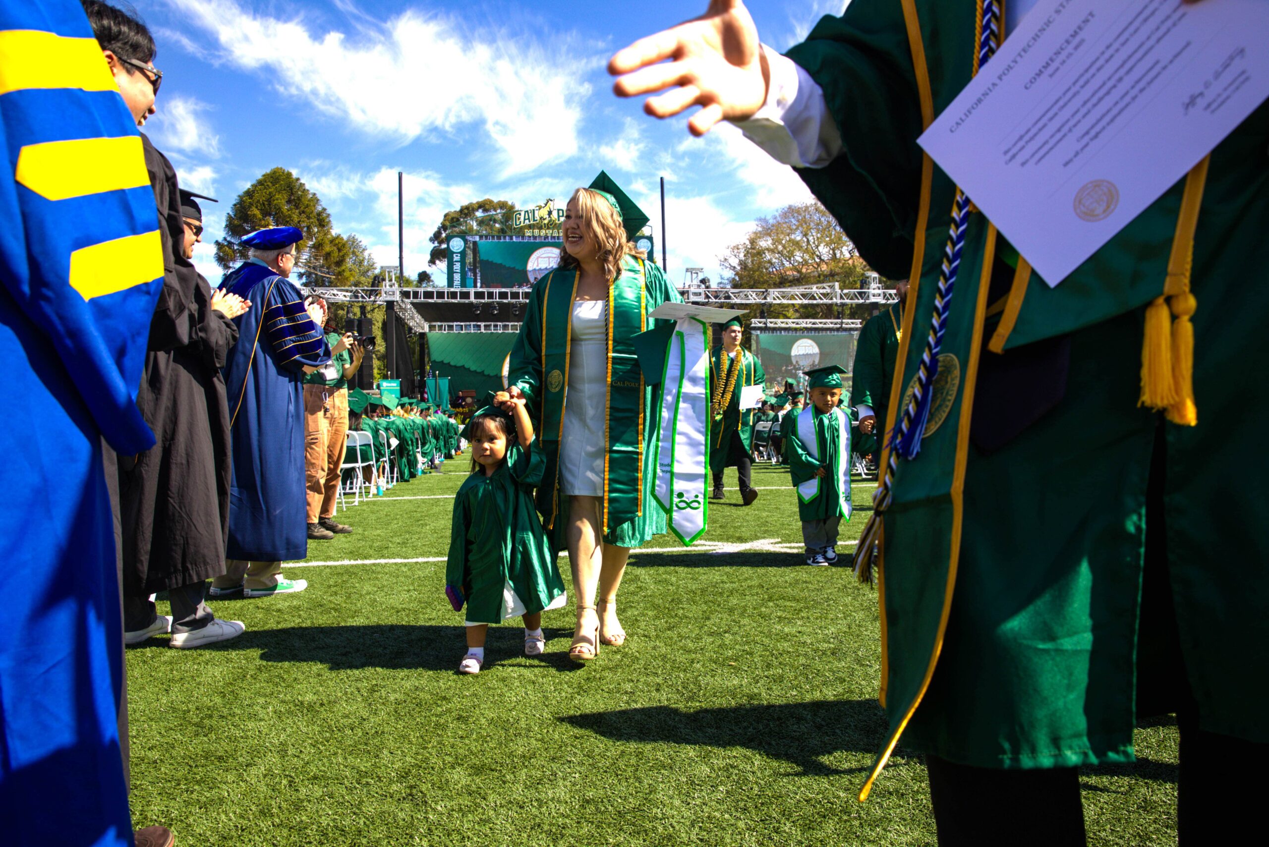 A student walks during commencement with a small child
