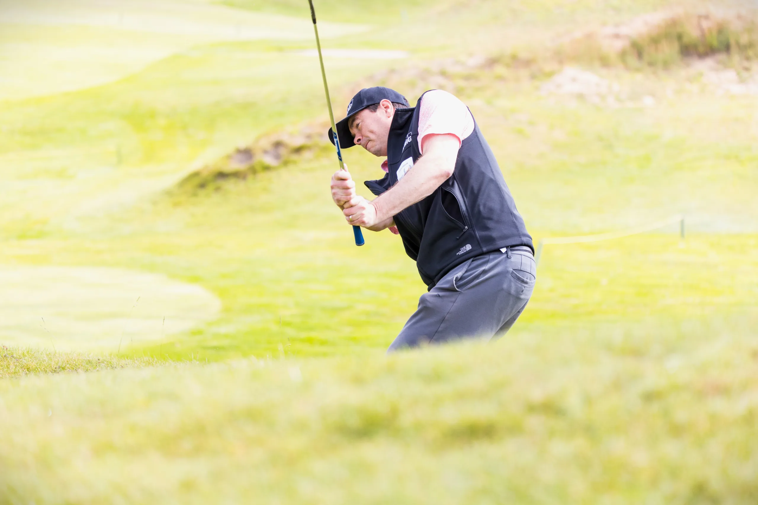 A golfer swing an iron near the green