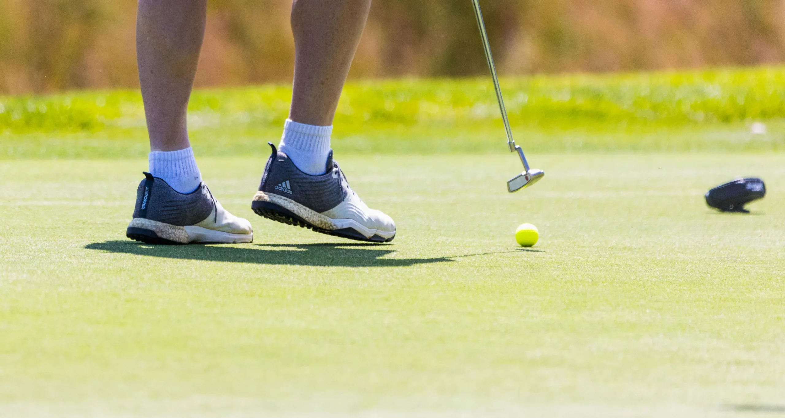 Detail shot of golf shoesm a club and a ball