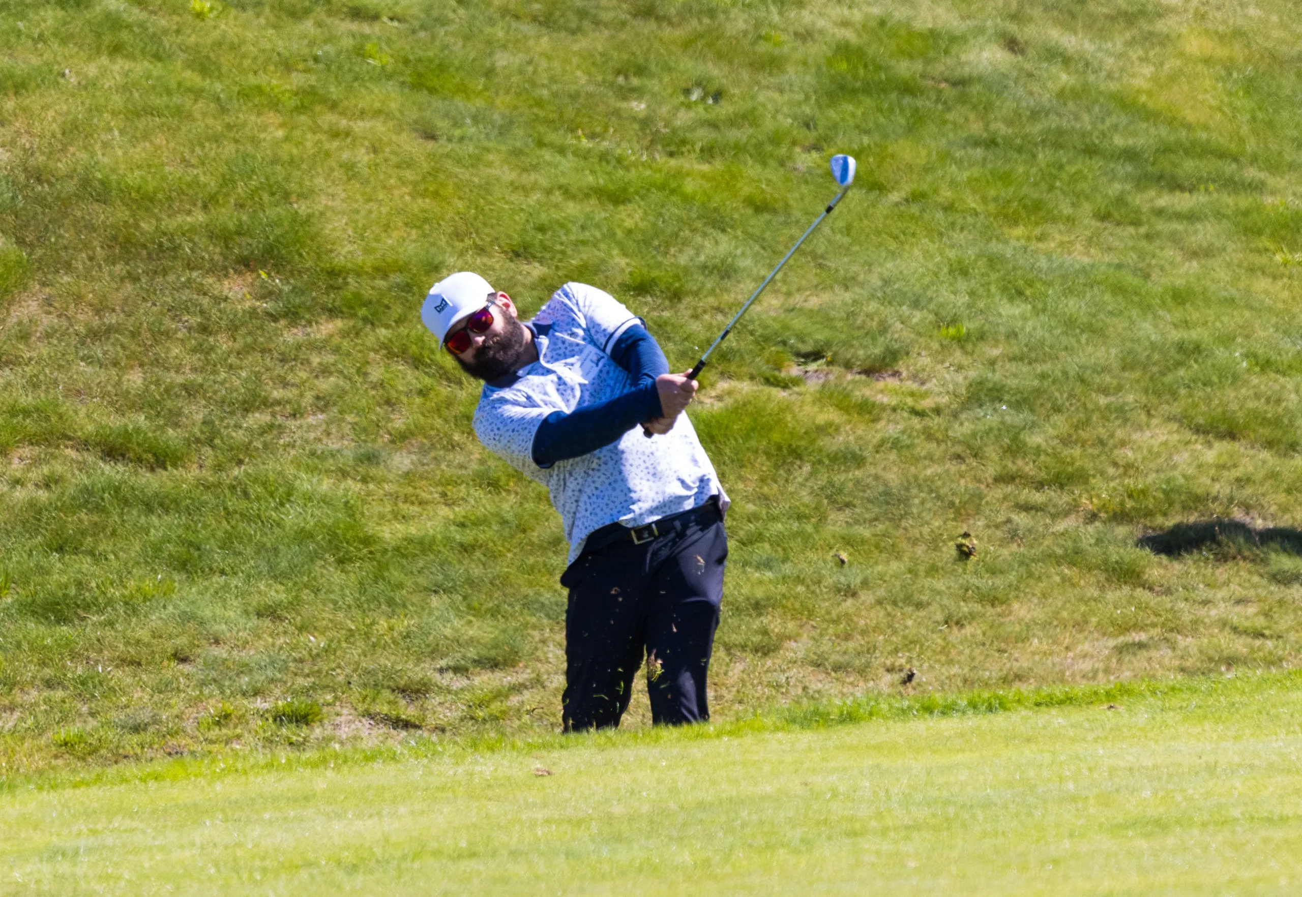 A golfer swing an iron club at his ball