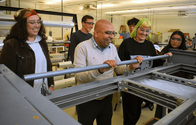 A faculty member observes a packaging machine with students in a packaging lab.