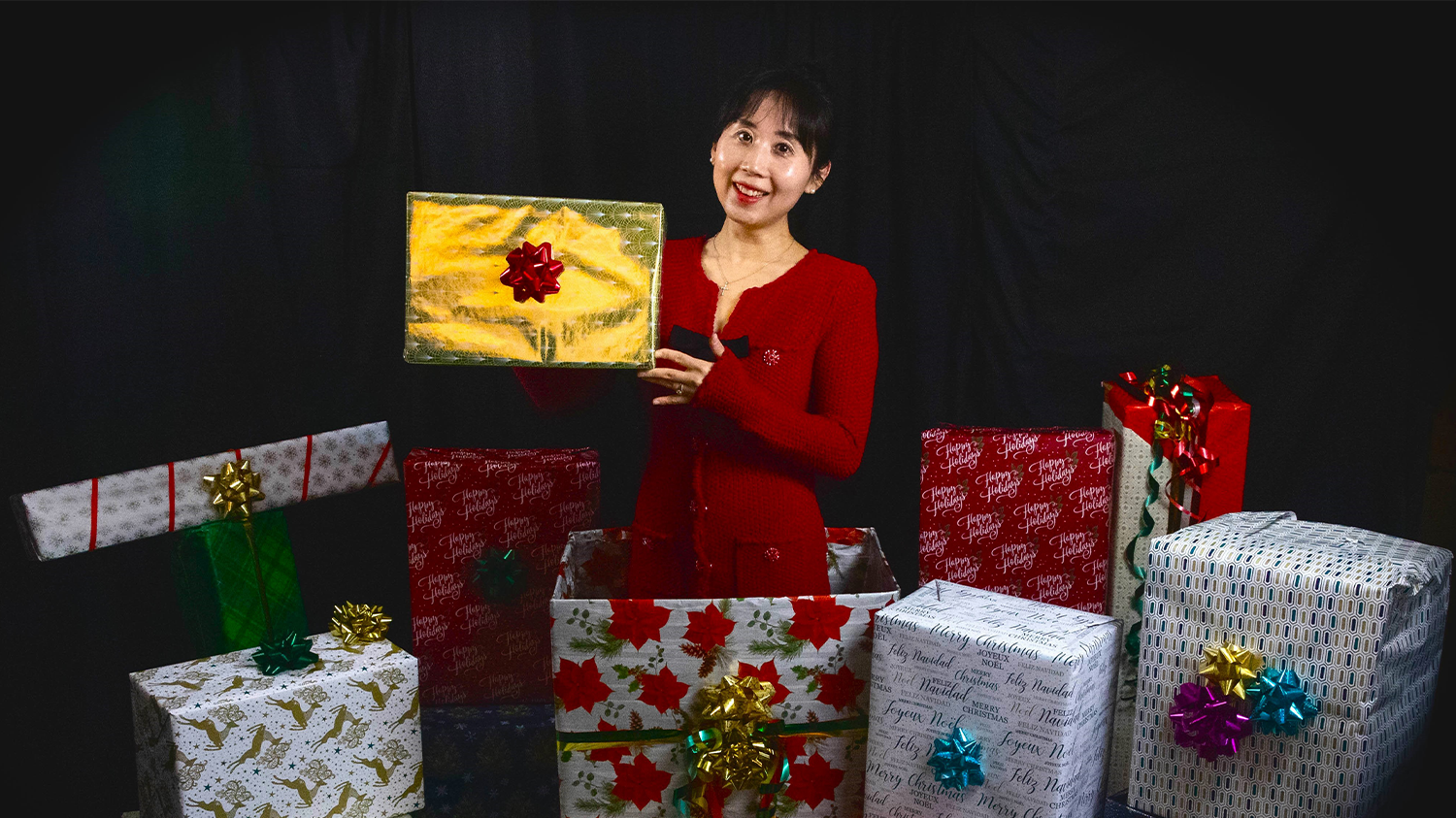 A marketing professor poses with several wrapped gift boxes in a studio