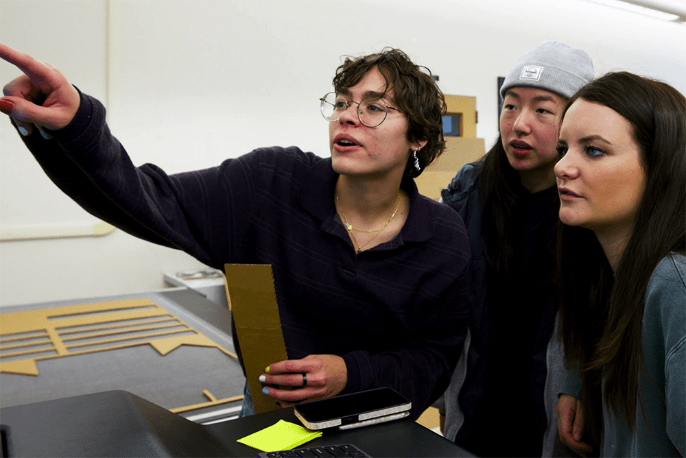 Three students look at a presentation board