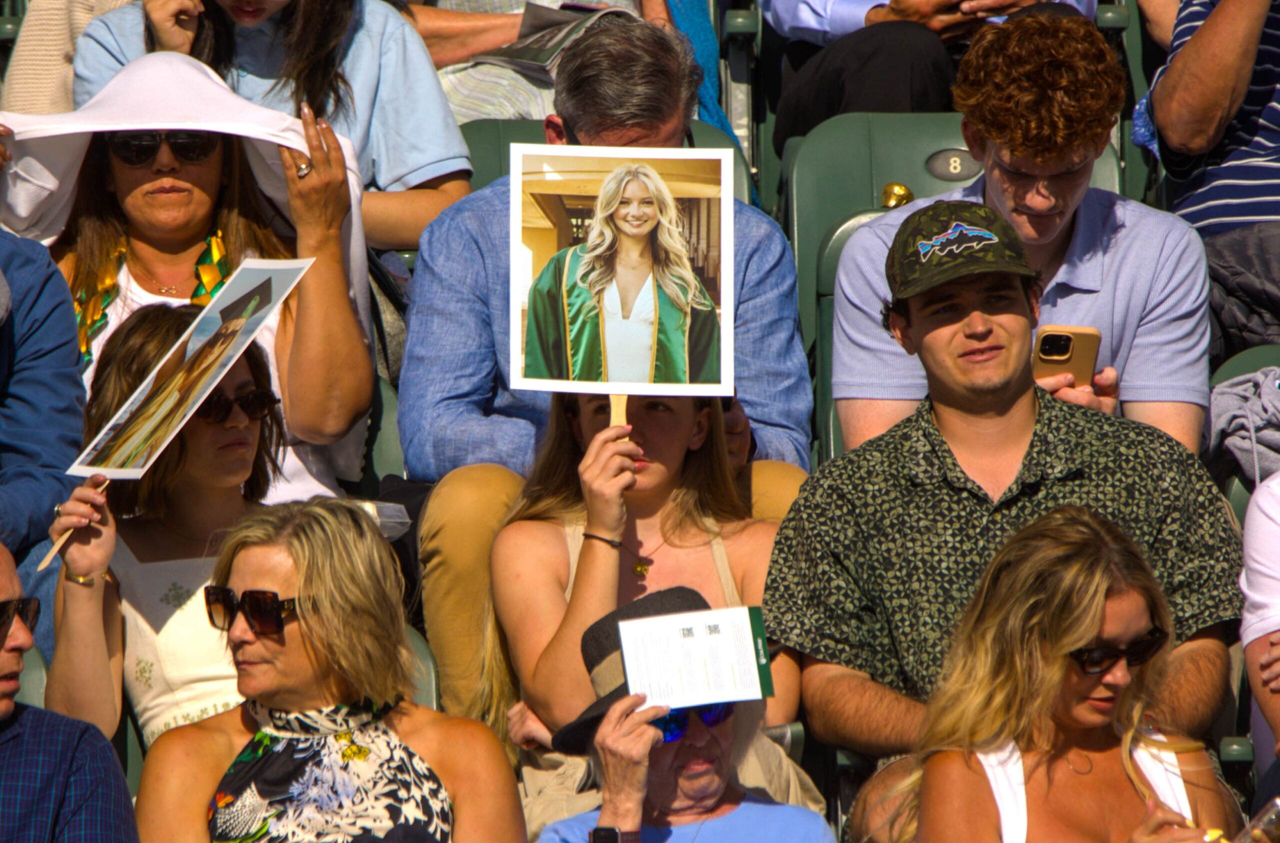 A member of the commencement crowd holds up a sign featuring their graduating loved one